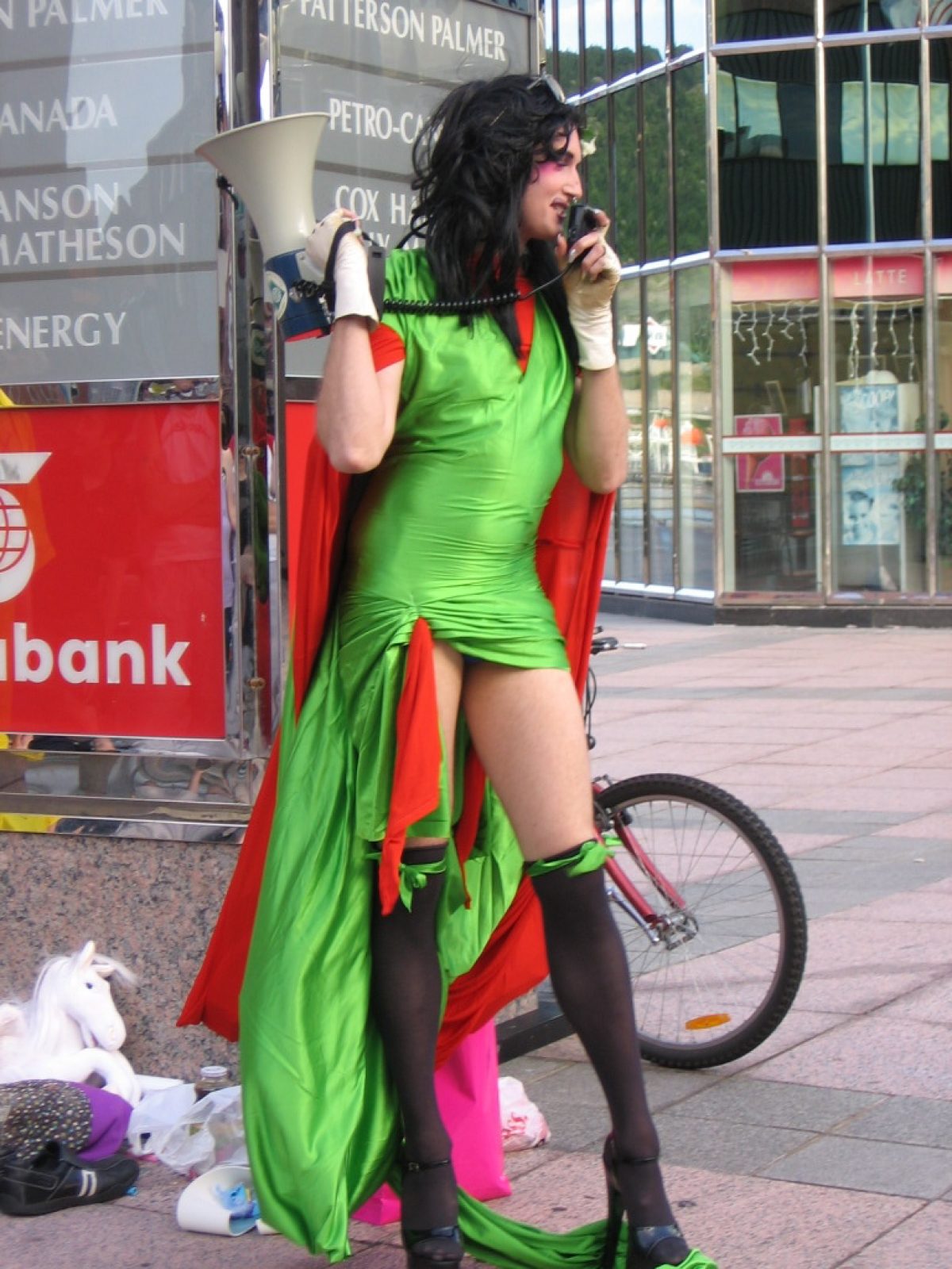 In a tight green dress with a train and bright red cape, Mikiki speaks into a megaphone as part of Drag Race X.