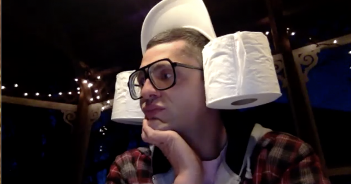 Jordan Arseneault as Peaches-LePoz, with large black rimmed glasses, facing slightly away from the camera, chin resting on hand, baseball cap with brim up and toilet paper rolls where ears might be.
