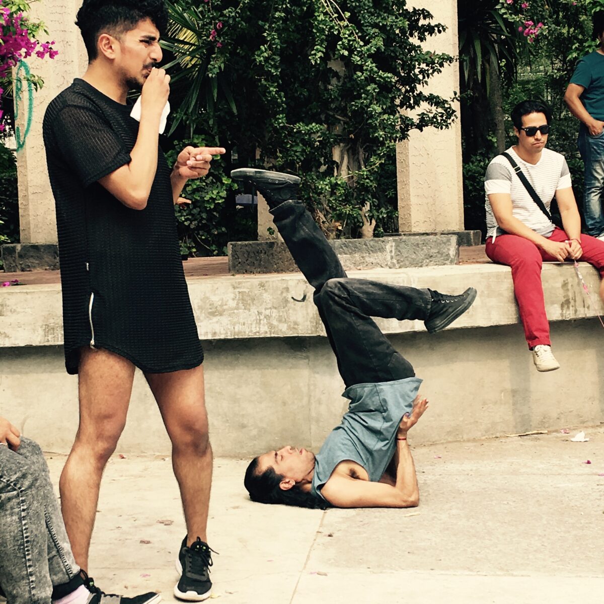 Jorge Nava of Apocalipstick (left side of image) and Héctor Victoria Vargas Payán/Vycktorya Letal Apocalipstick LaBeija (centre, performing a ballroom dance move, on his back on the ground with legs in the air), outdoors in the Parque Mexico, at an Apocalipstick Open House public rehearsal.