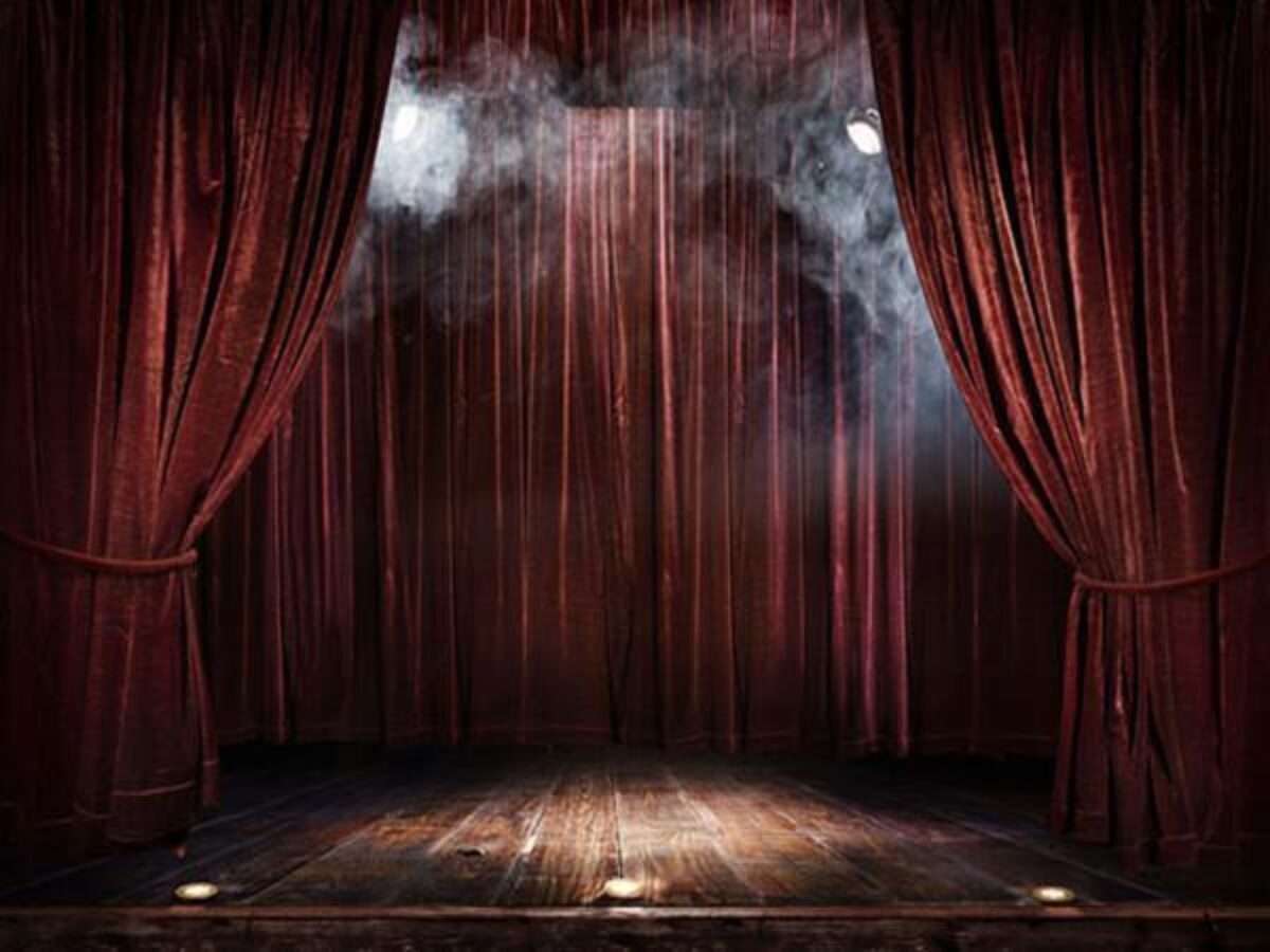 An empty stage with red velvet curtains, stage lights and smoke.